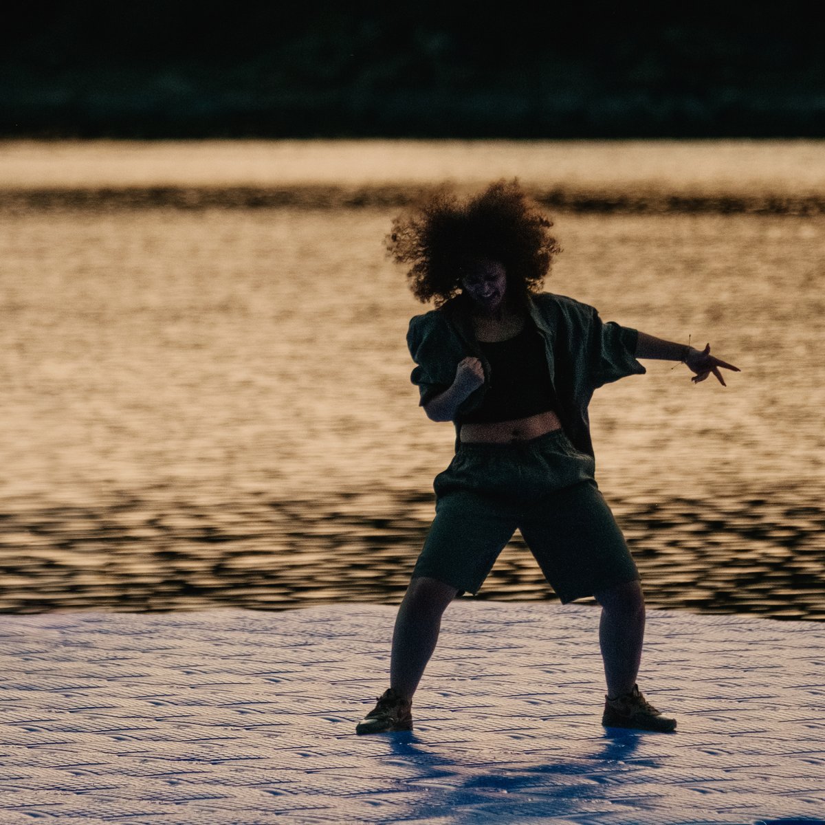 A dancer on a pontoon by the water, in evening light